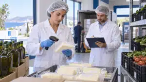 Food quality specialists checking sealed cheese deliveries beside olive oil and produce in a supermarket receiving area