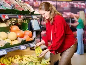 Shopper holding a bunch of bananas beside a Lidl fruit and vegetable display