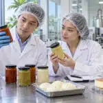 Food technologists assessing sauce samples alongside steamed buns and a packaged cake in a development kitchen