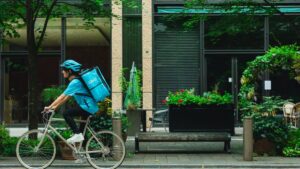 A helmeted cyclist rides a bicycle carrying a turquoise Wolt delivery bag.