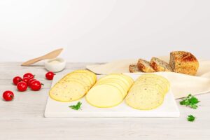 Slices of cheese on a white board with bread, tomatoes and butter
