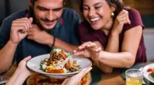 Two diners looking at a plate of food served at a table.