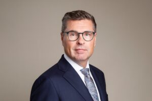Jorma Rauhala wearing glasses, a dark suit and a patterned tie