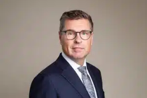 Jorma Rauhala wearing glasses, a dark suit and a patterned tie