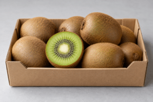 Whole brown kiwifruit and a halved green kiwifruit in a cardboard tray on a pale surface.