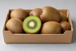 Whole brown kiwifruit and a halved green kiwifruit in a cardboard tray on a pale surface.