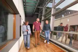 Three people walking through a glass-sided office corridor