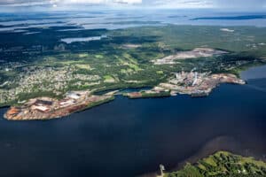 Aerial view of a paper mill beside water and forest at Munksund.